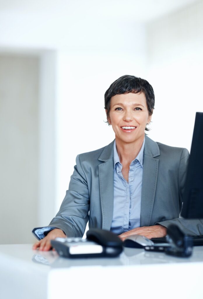 Mature business woman at office desk. Portrait of mature business woman smiling at office desk.